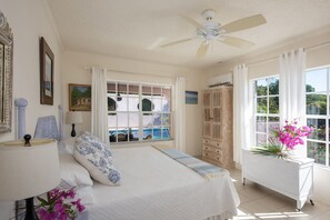 Relax in this serene bedroom with a large bed, ceiling fan, and a window offering a view of the pool and lush surroundings.