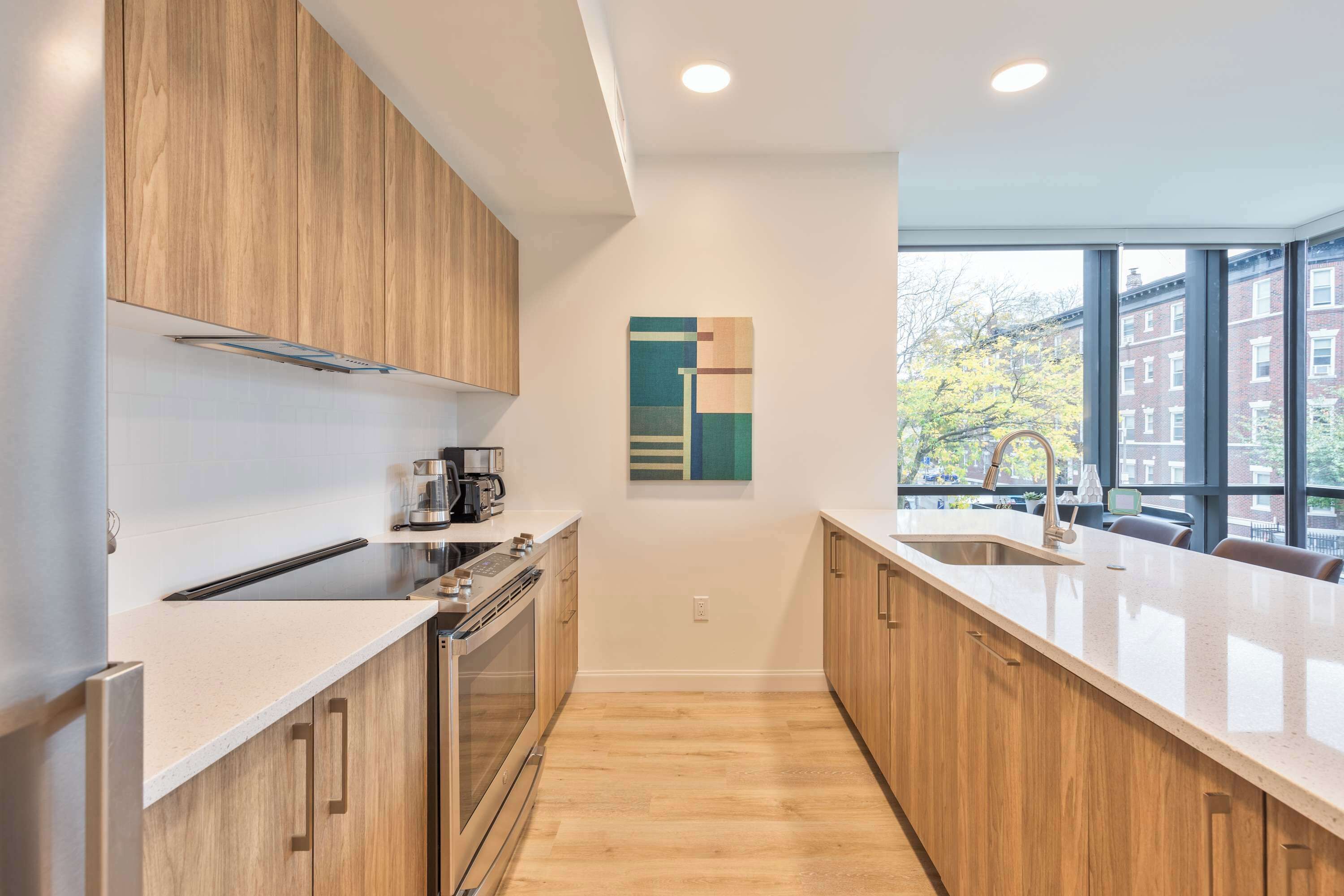 A modern kitchen with wooden cabinets, a stainless steel range, and a large window providing a view of the outside.