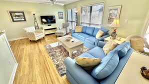 Un salon avec un canapé bleu, une table basse blanche, un téléviseur et un ventilateur de plafond.