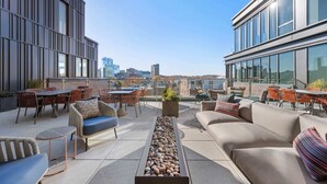 A rooftop terrace with outdoor seating, a fire feature, and a city view.