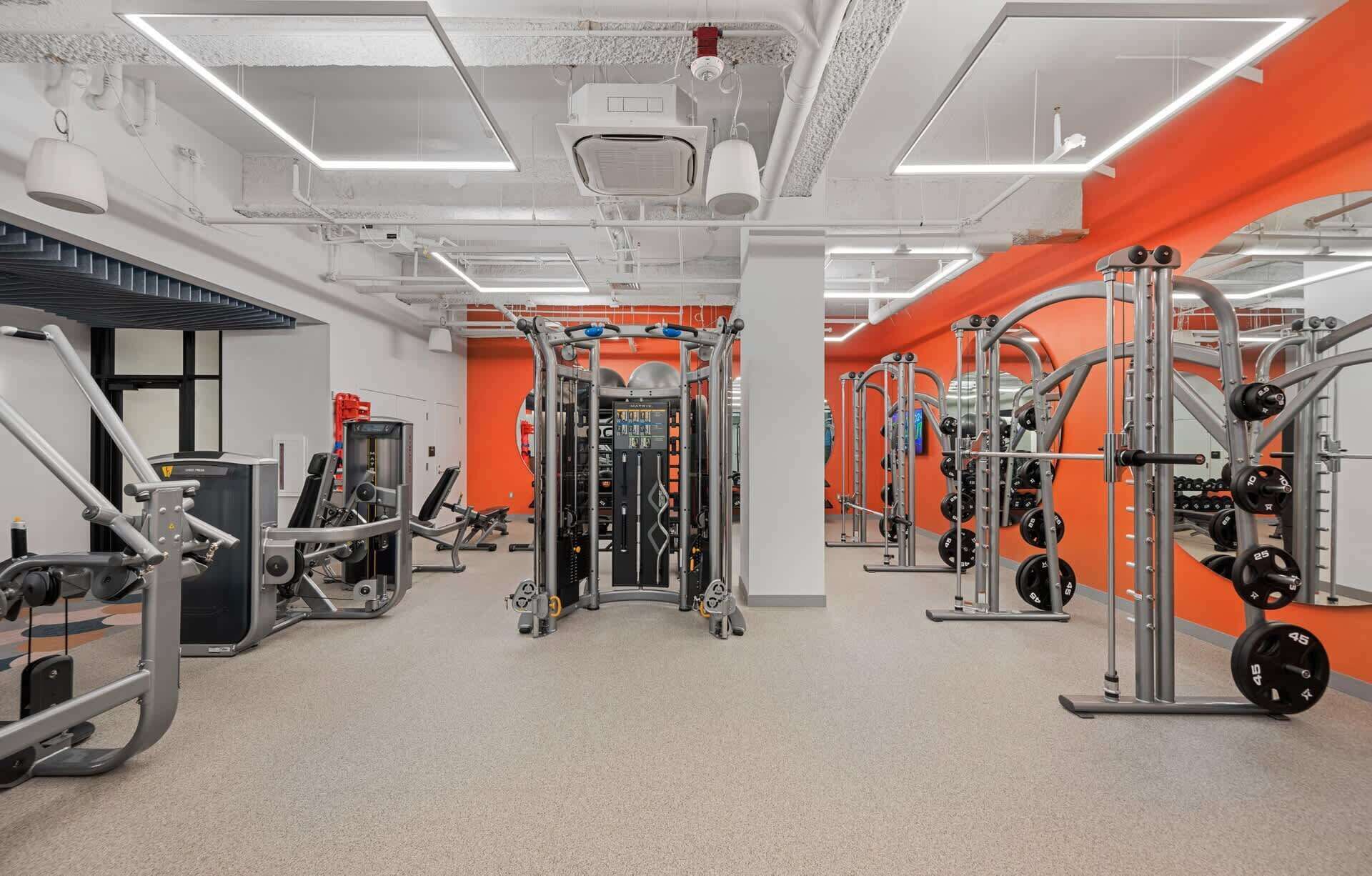 A gym with various exercise machines, weight racks, and a mirrored wall.