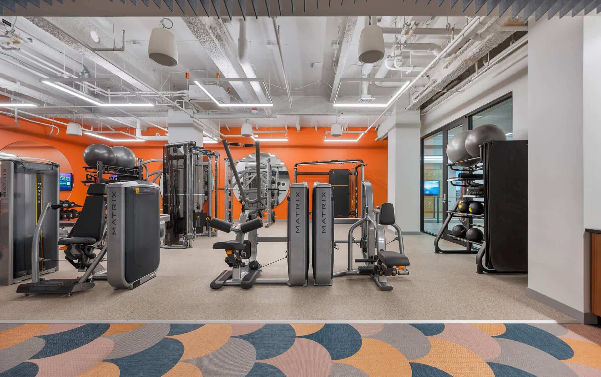 A gym with various exercise equipment, including treadmills, weight machines, and a rack of dumbbells.