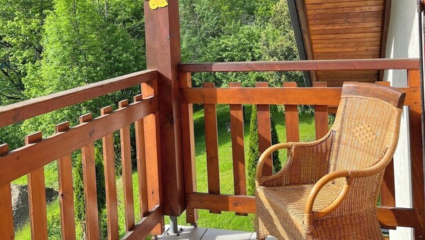 A wooden balcony with a wicker chair, a wooden railing, and a view of green mountains. - CHARMING CHALET - SLEEPS 6 (Allemont)