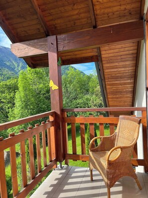 A wooden balcony with a wicker chair, a wooden railing, and a view of green mountains. - CHARMING CHALET - SLEEPS 6 (Allemont)