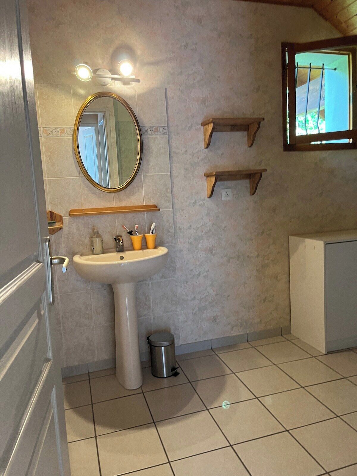 Ein Badezimmer mit einem Standwaschbecken, einem runden Spiegel und Holzregalen.