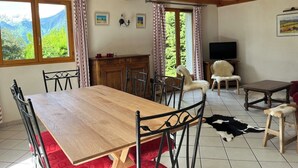 A dining area with a wooden table and chairs, a chandelier, and a view of mountains through large windows. - CHARMING CHALET - SLEEPS 6 (Allemont)