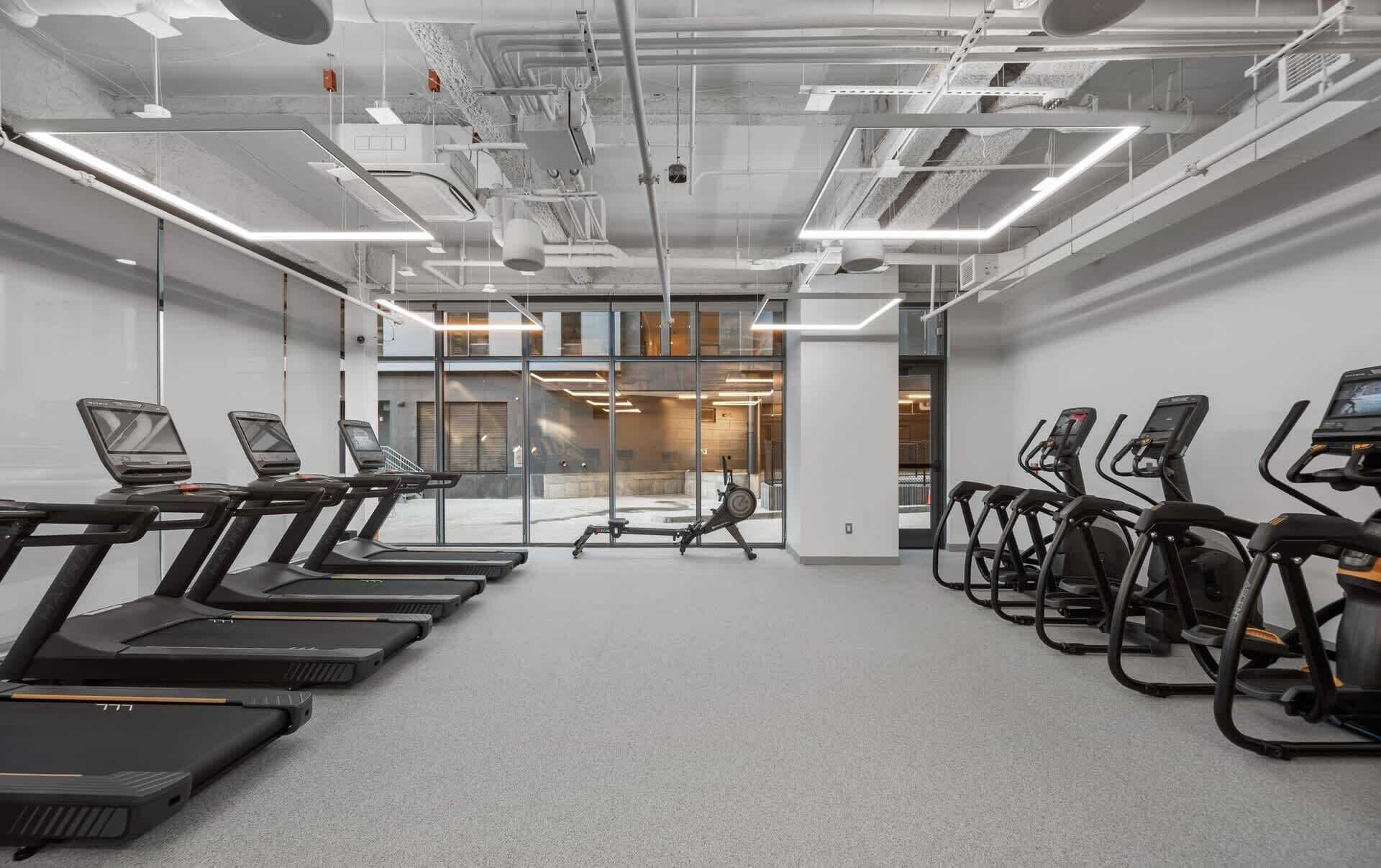 Ein Fitnesscenter mit Laufbändern und Crosstrainern, großen Fenstern und modernem Design.