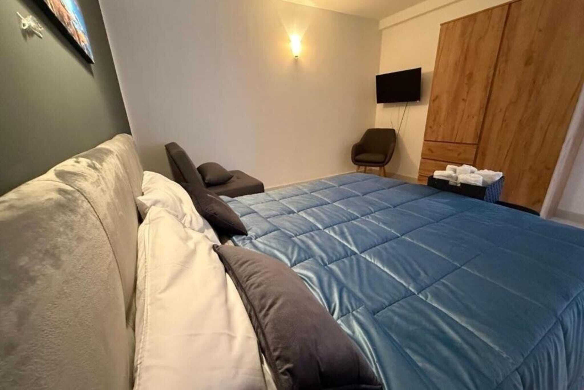 A bedroom with a bed, a chair, a wardrobe, and a TV.