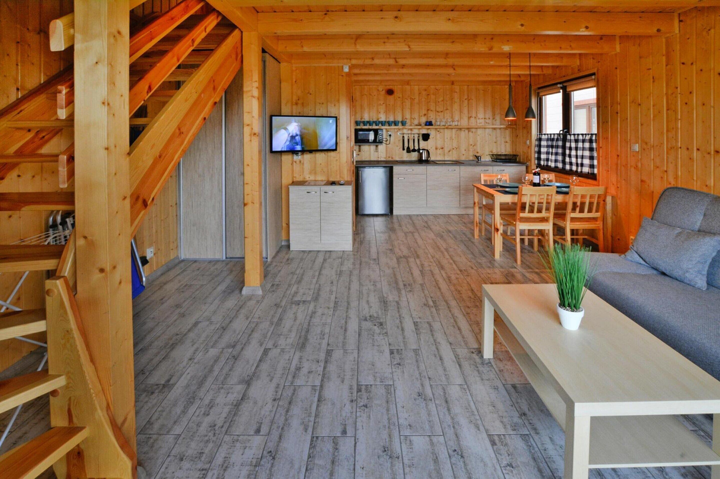 A wooden cabin interior with a dining area, kitchen, and living room.
