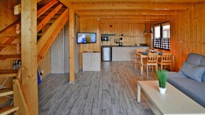 A wooden cabin interior with a dining area, kitchen, and living room. - Holiday Home in Sianozety Near Beach (Ustronie Morskie)