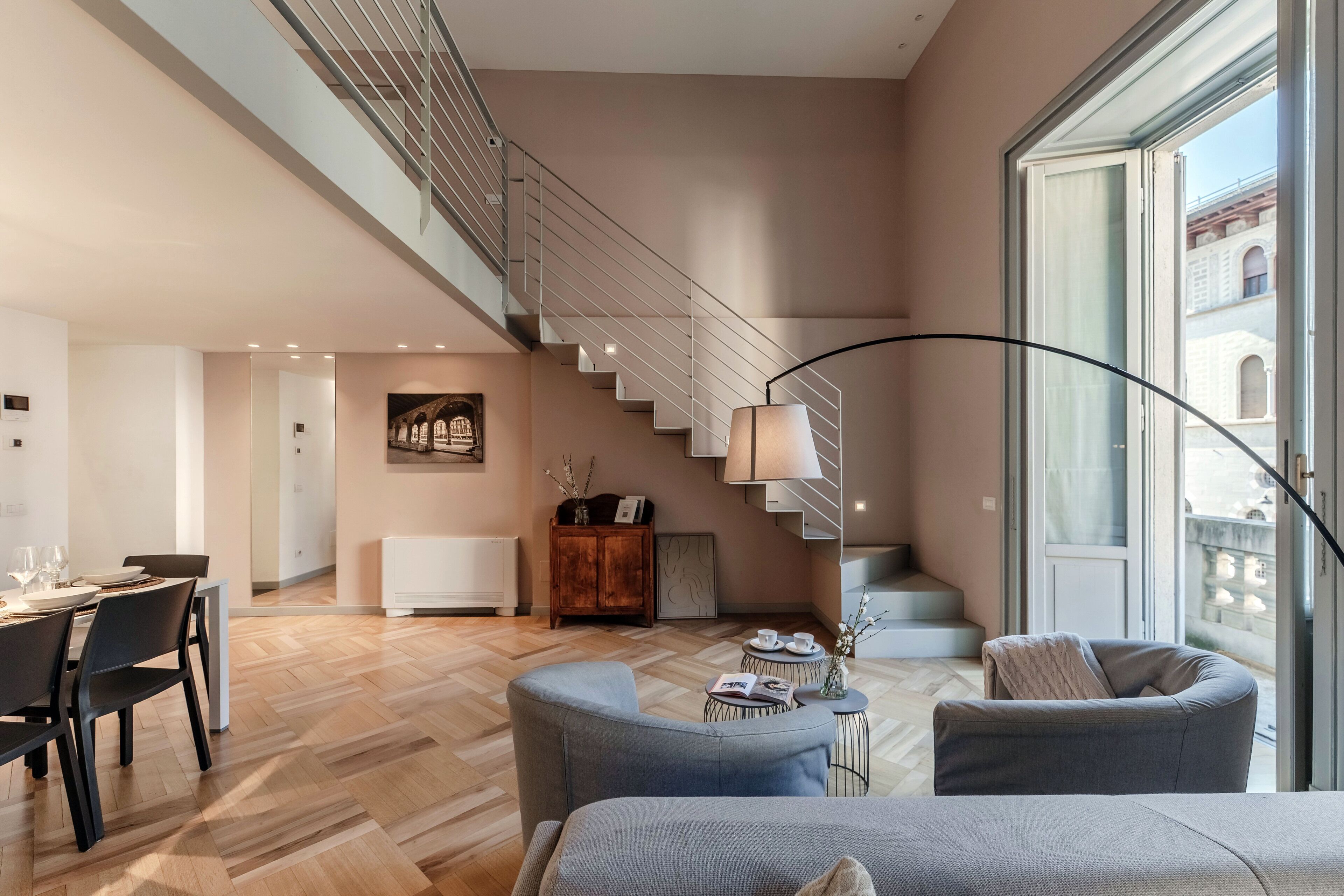 A modern living room with a staircase, a dining area, and a view of the city.
