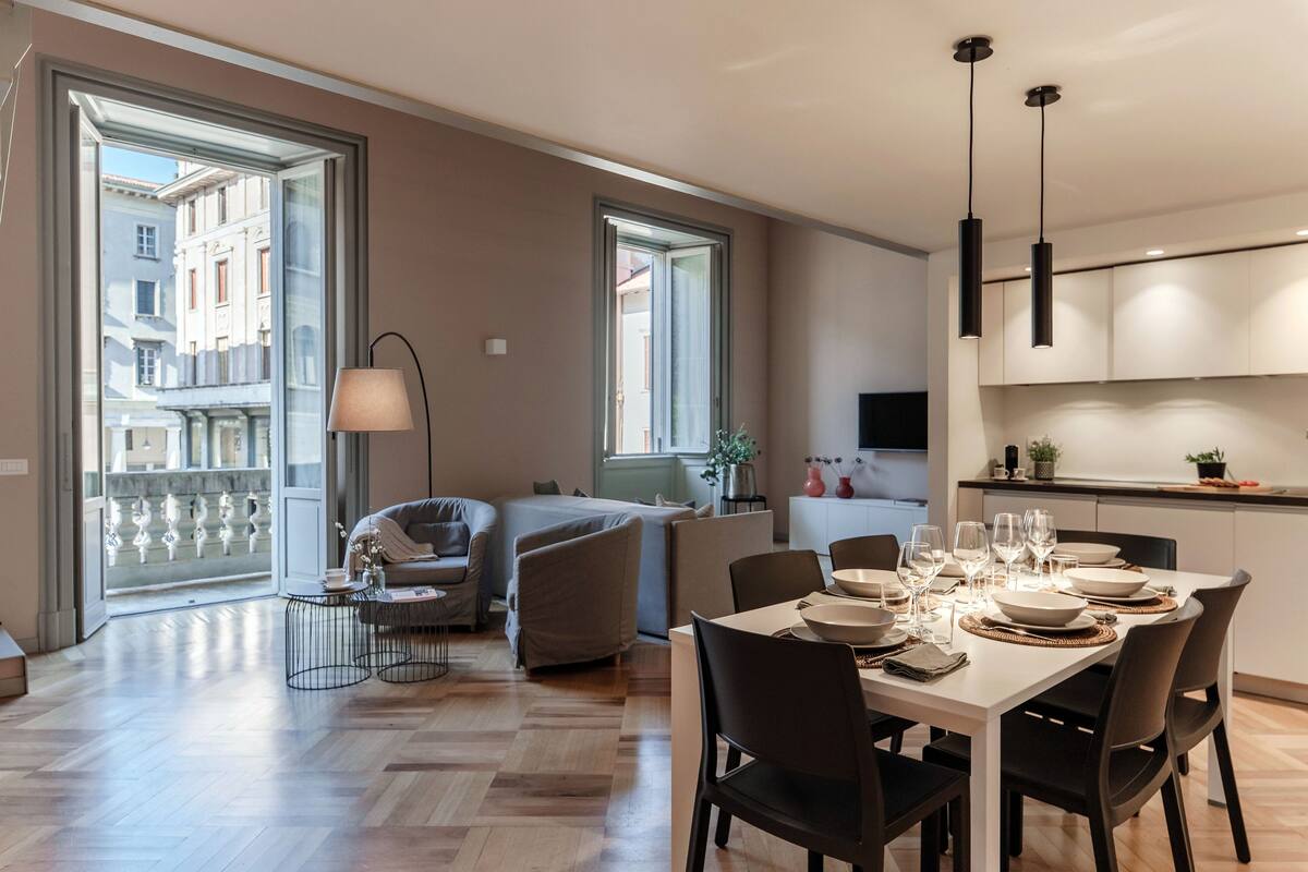 A modern apartment with a dining area, a sofa, a lamp, and large windows.