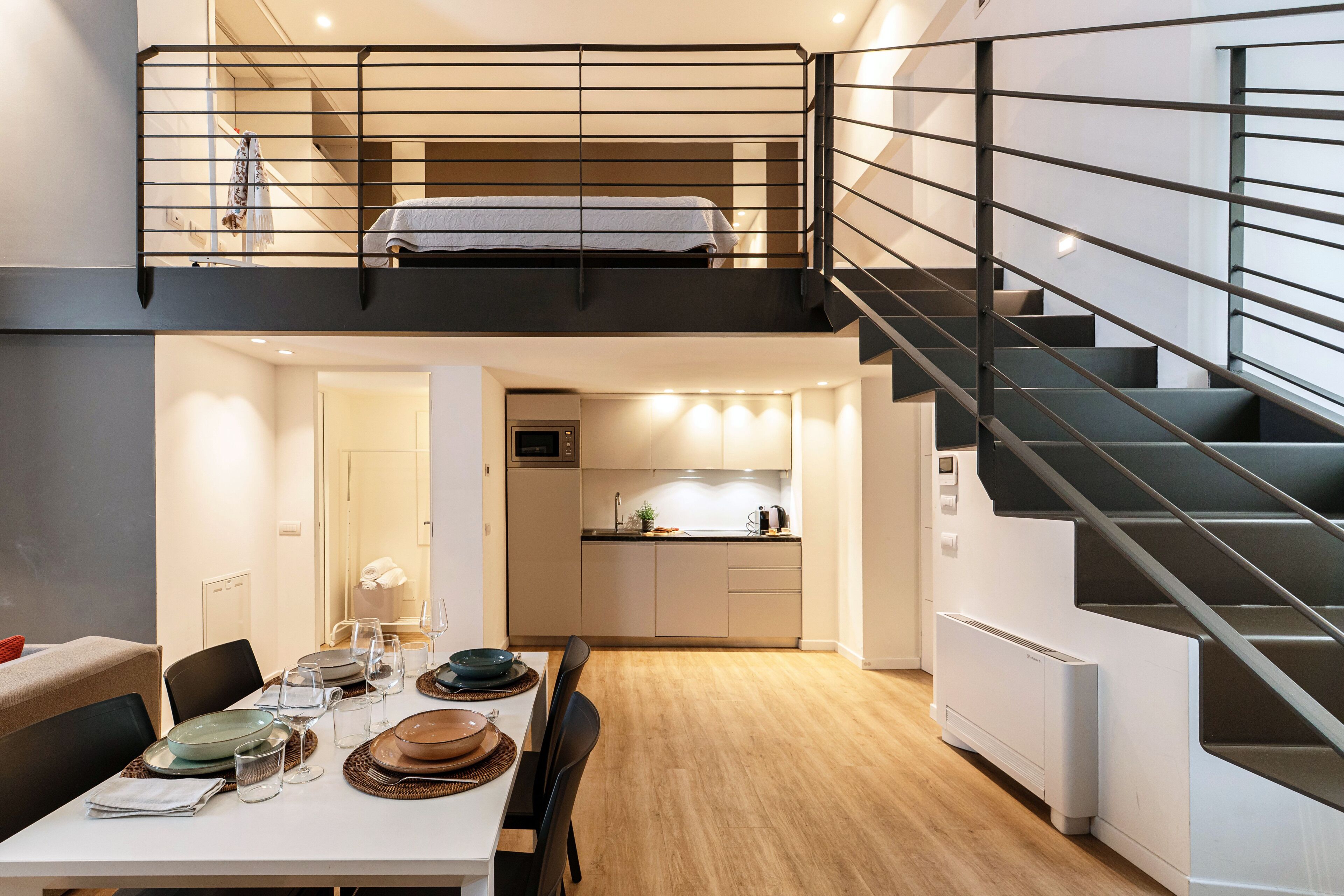 Un appartement moderne de style « loft », comprenant un coin repas, une cuisine et un escalier menant à une chambre située en mezzanine.