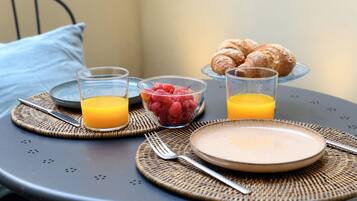 Desayuno con croissants, un tazón de frambuesas y vasos de jugo de naranja sobre una mesa redonda.