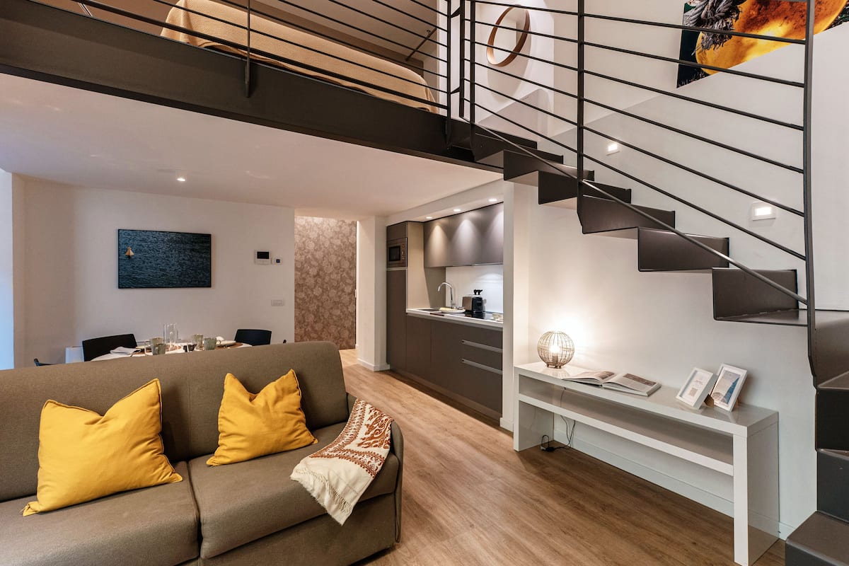 A modern living room with a sofa, a staircase, and a kitchen area.