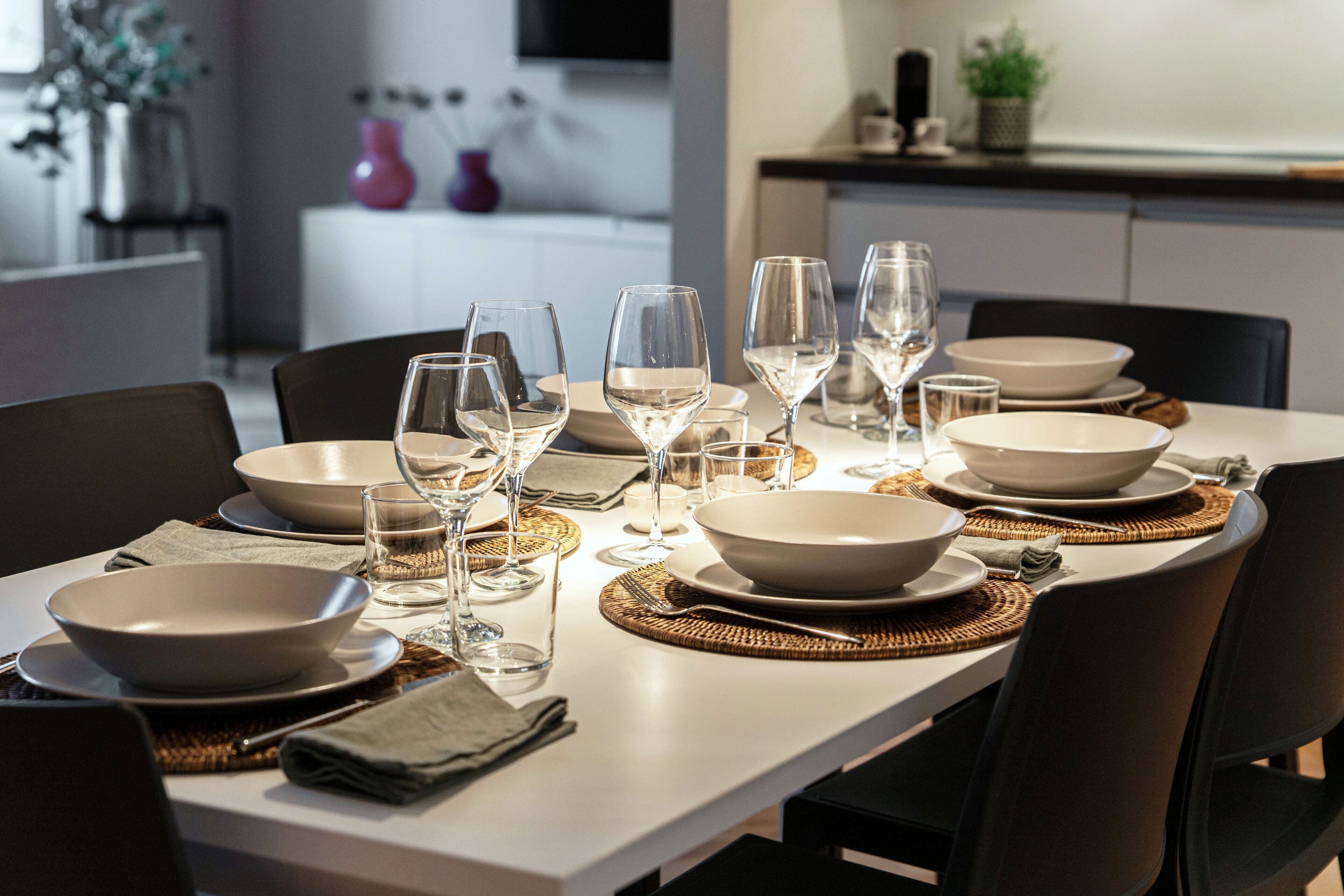 Una mesa de comedor dispuesta con fuentes, vasos y cubiertos, rodeada de sillas.
