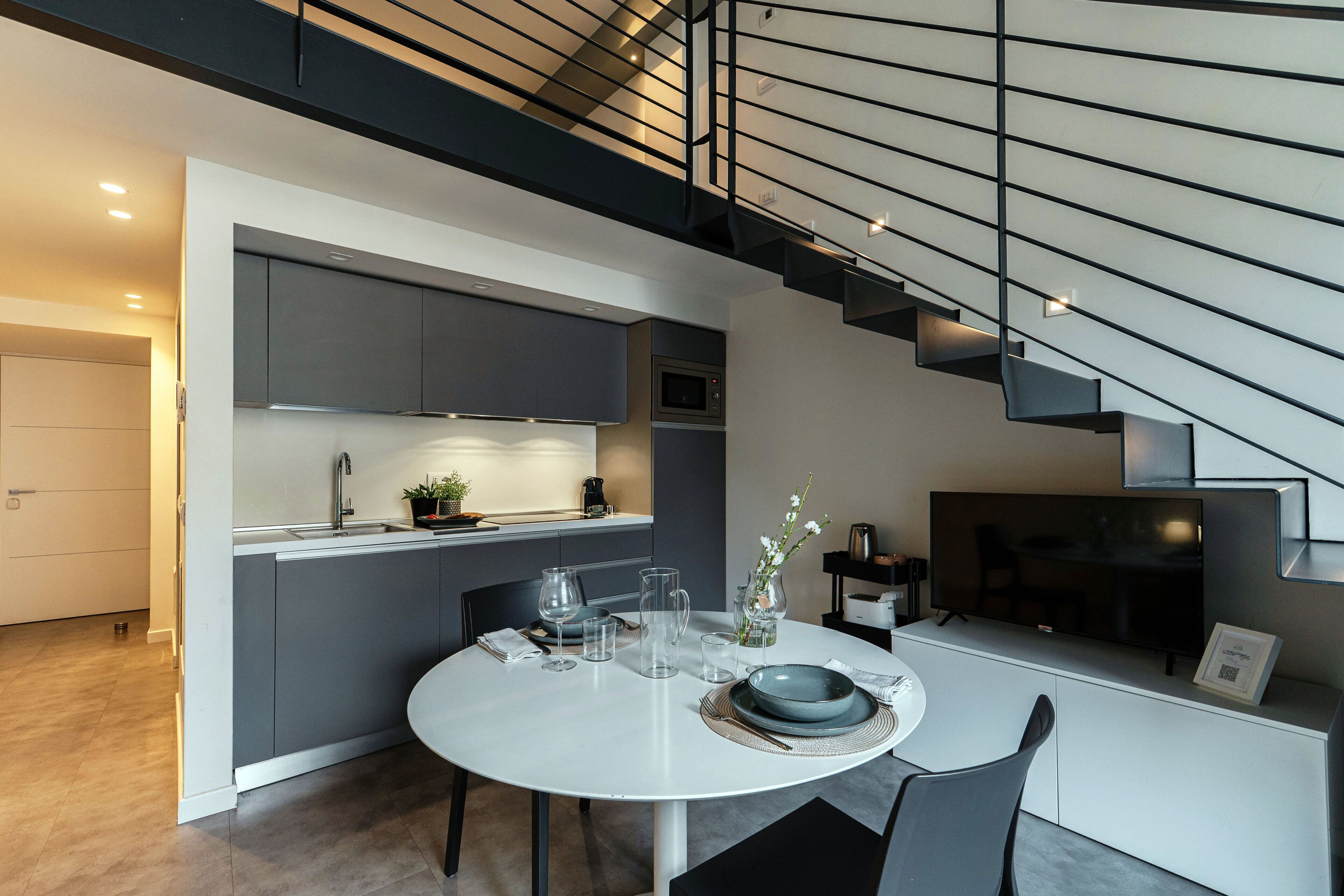 A modern kitchen with grey cabinets, a dining table set with plates, glasses, and a vase with flowers.