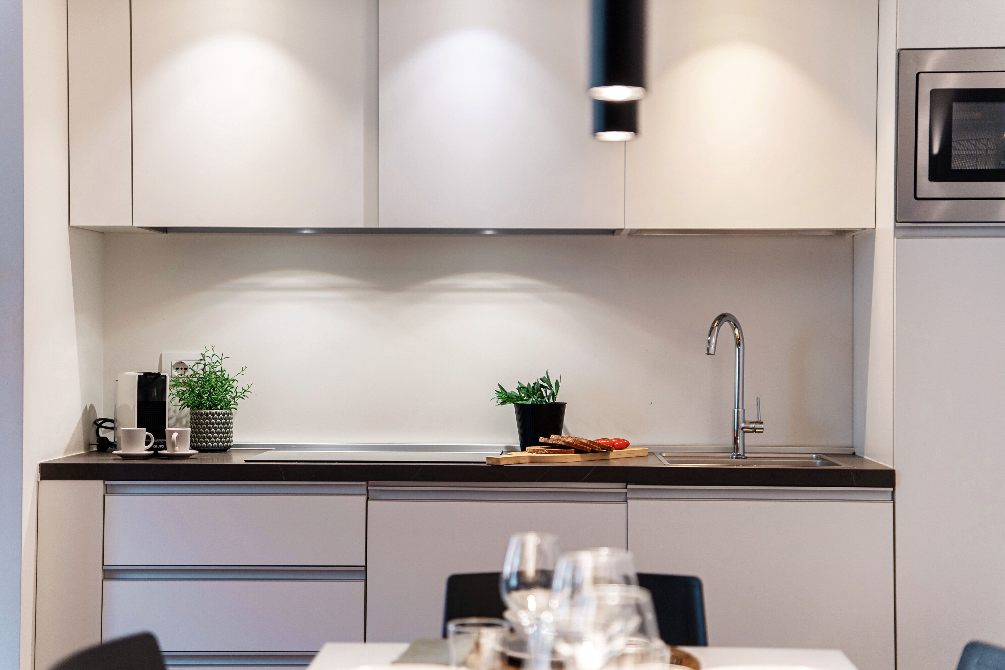 Una cocina moderna con horno empotrado, pileta y comedor con sillas y mesa.