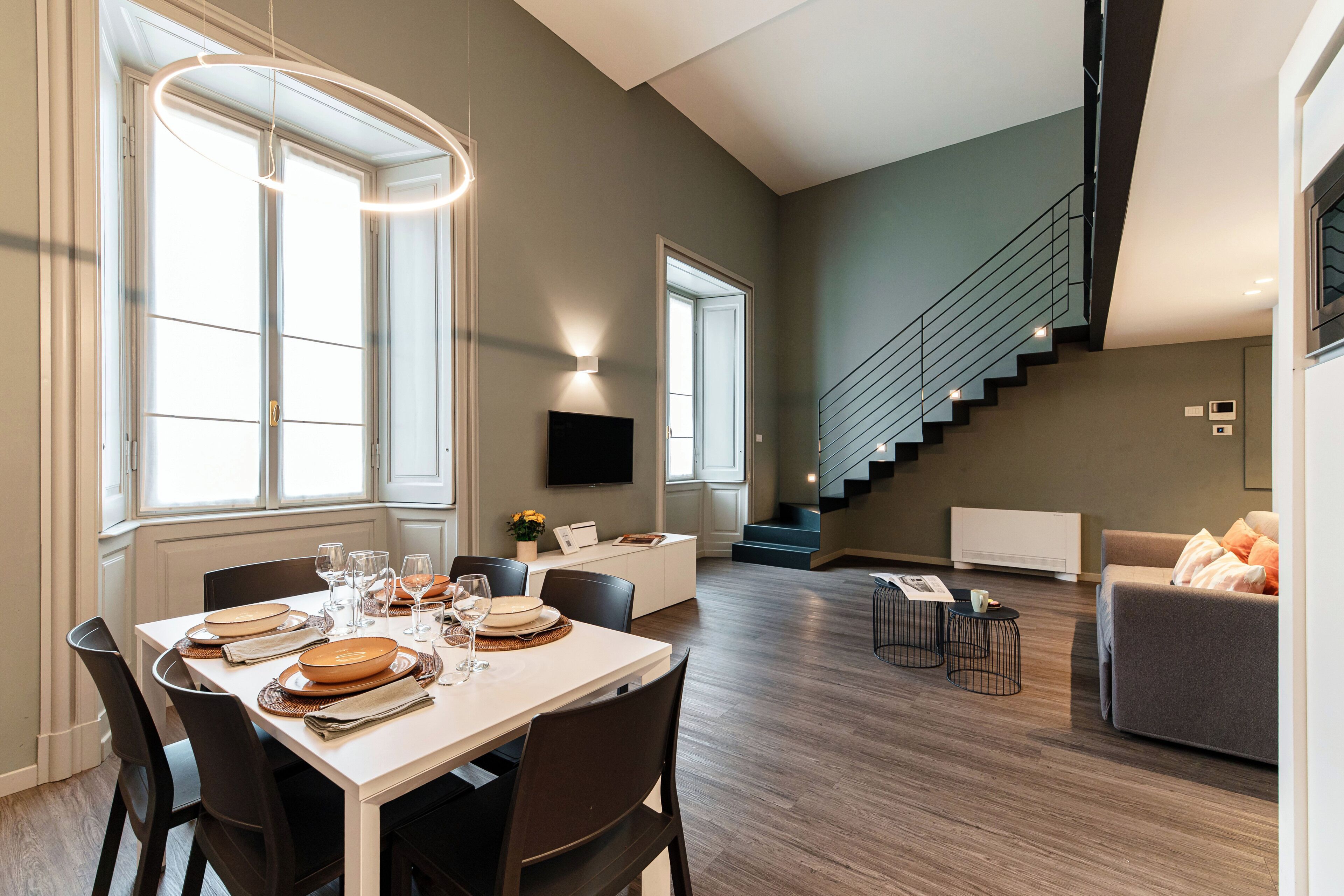 A modern living room with a dining area, a staircase, and a flat-screen TV.