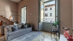 Ein modernes Wohnzimmer mit einem grauen Sofa, einer Treppe und einem großen Fenster mit Blick auf ein Gebäude.