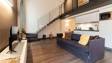 A modern living room with a sofa, a flat-screen TV, a staircase, and a kitchen area.