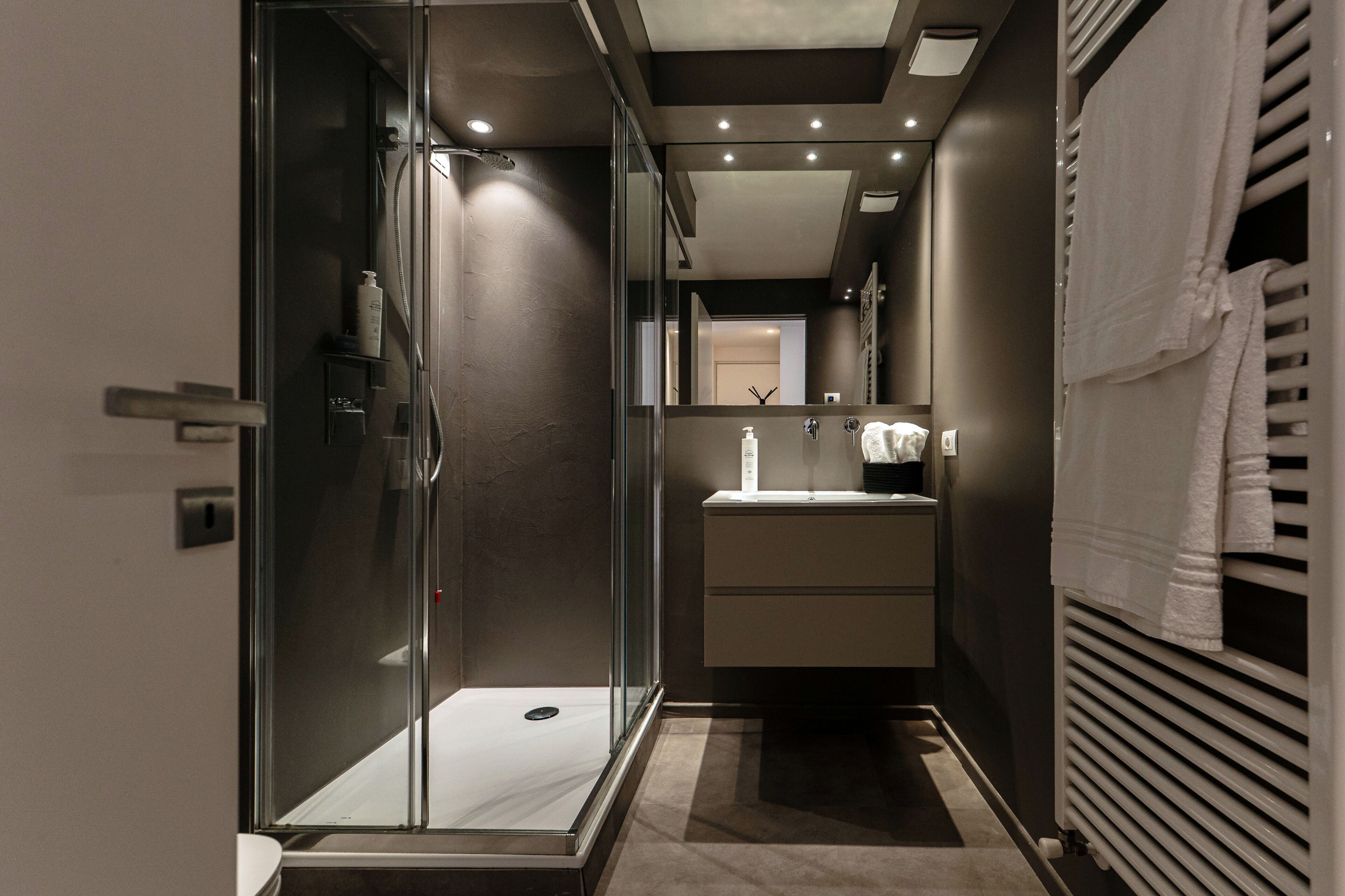 Un baño moderno con cabina de ducha de vidrio, lavamanos y perchero.