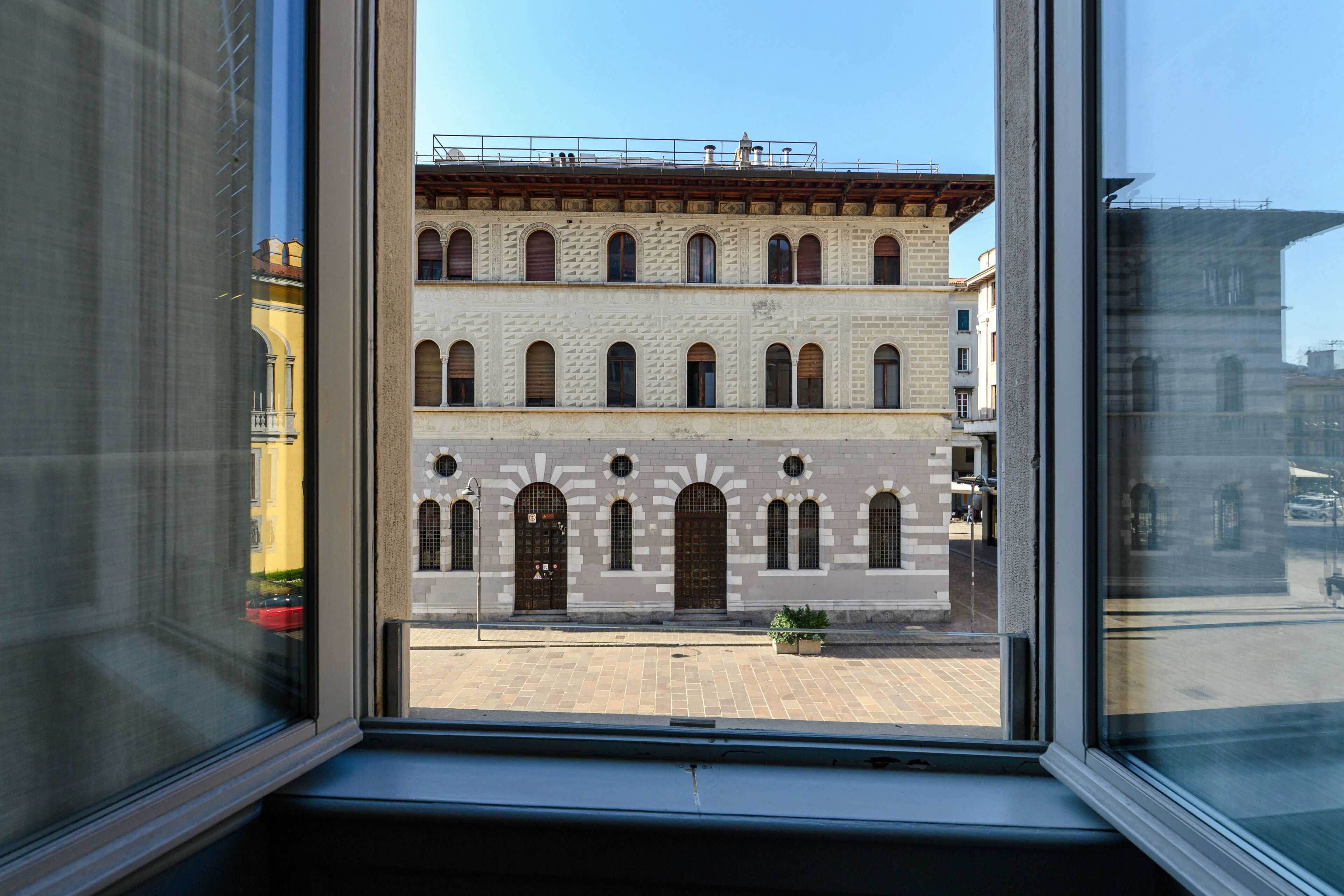 A view through a window of a building with multiple floors, large arched windows, and a brick facade.