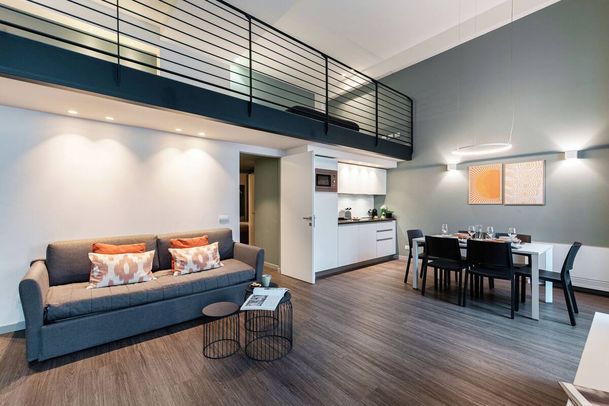 A modern apartment with a loft-style kitchen, a dining area, and a living room with a sofa and coffee table.