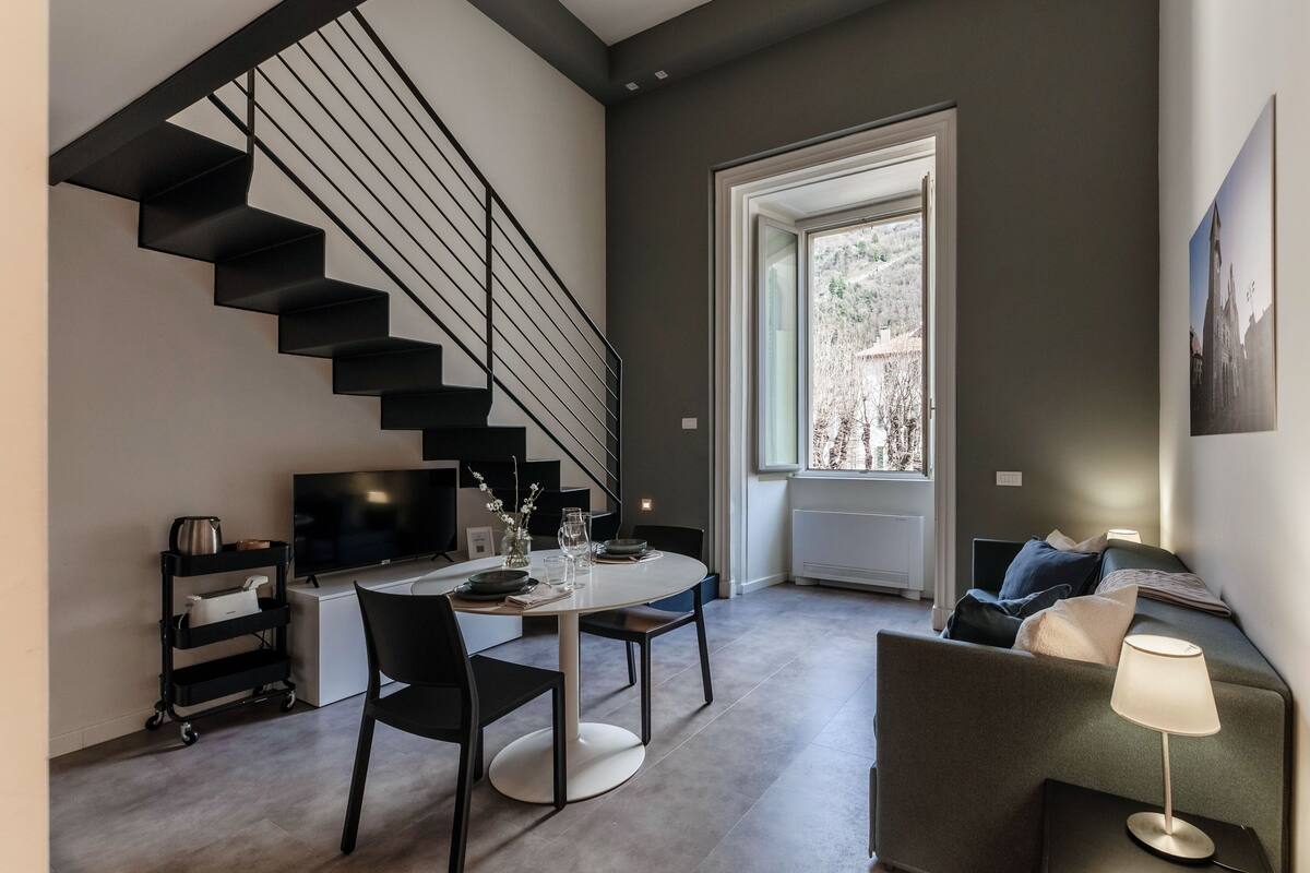 A modern living space with a staircase, a dining area, a sofa, a TV, and a window with a view.
