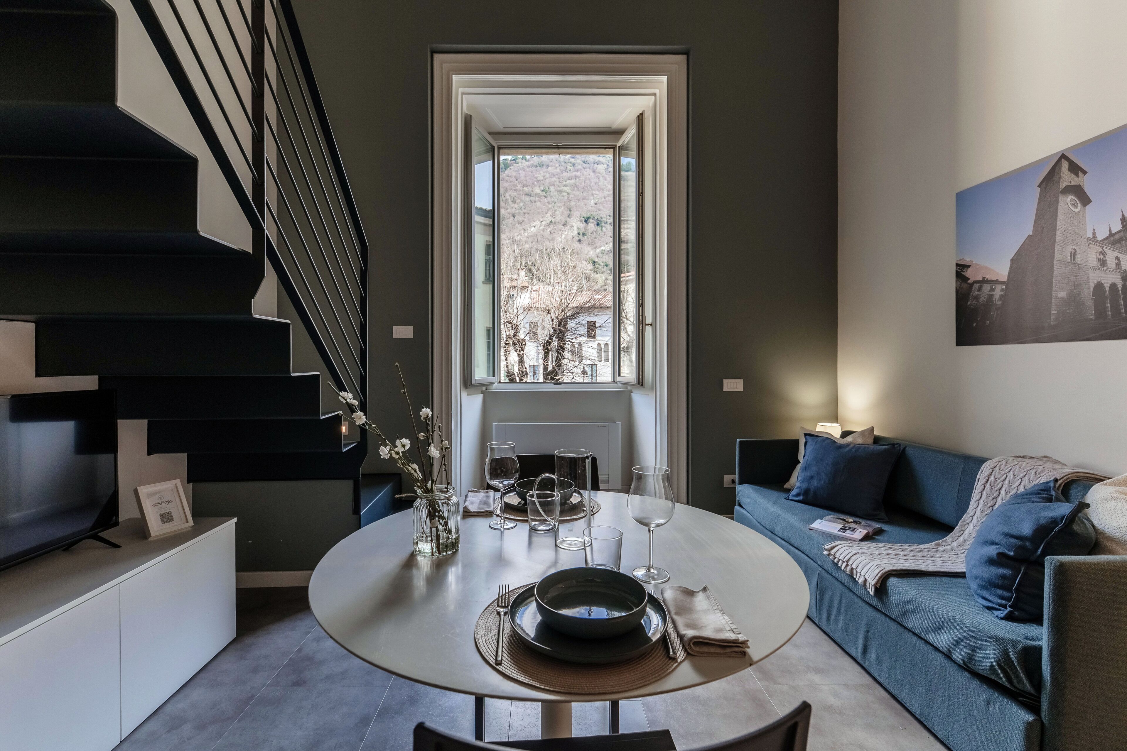 Una sala de estar moderna con comedor, una escalera y vistas por una ventana.