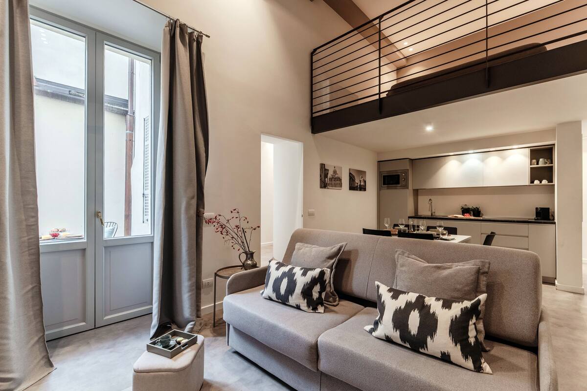 A modern living room with a grey sofa, a small side table, and a view of a kitchen.