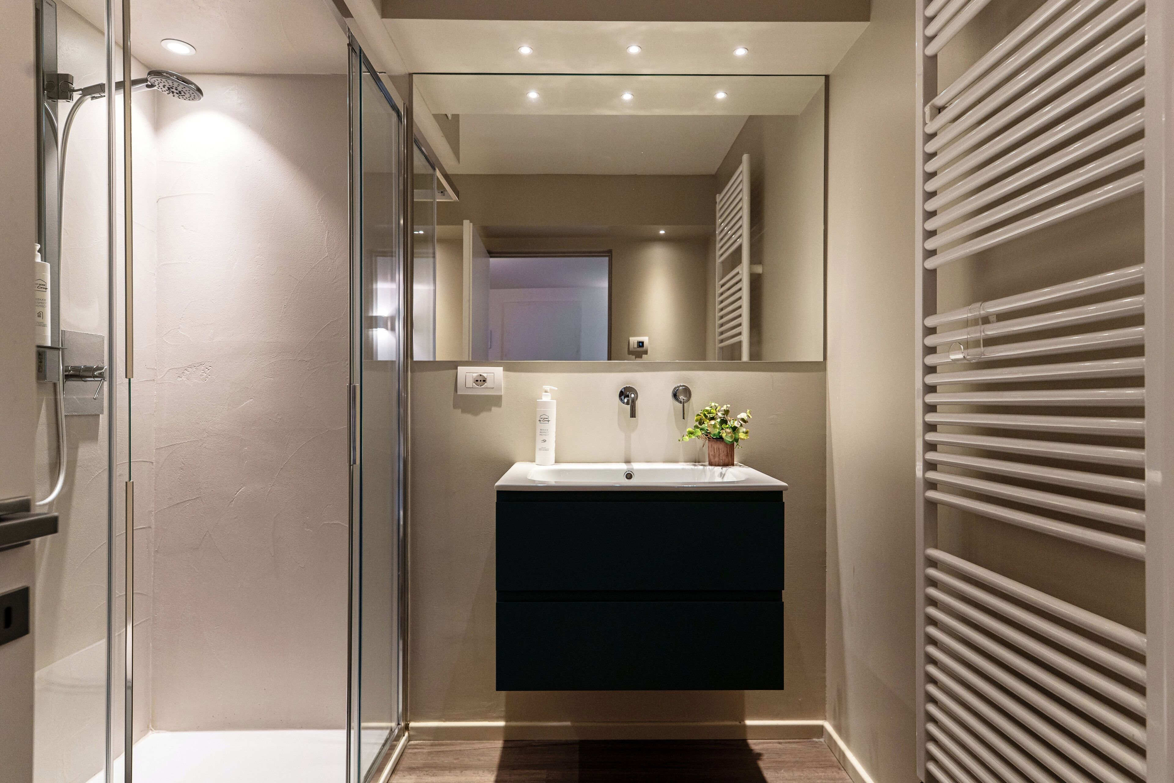 Un baño moderno con cabina de ducha de vidrio, tocador oscuro, espejo y perchero.