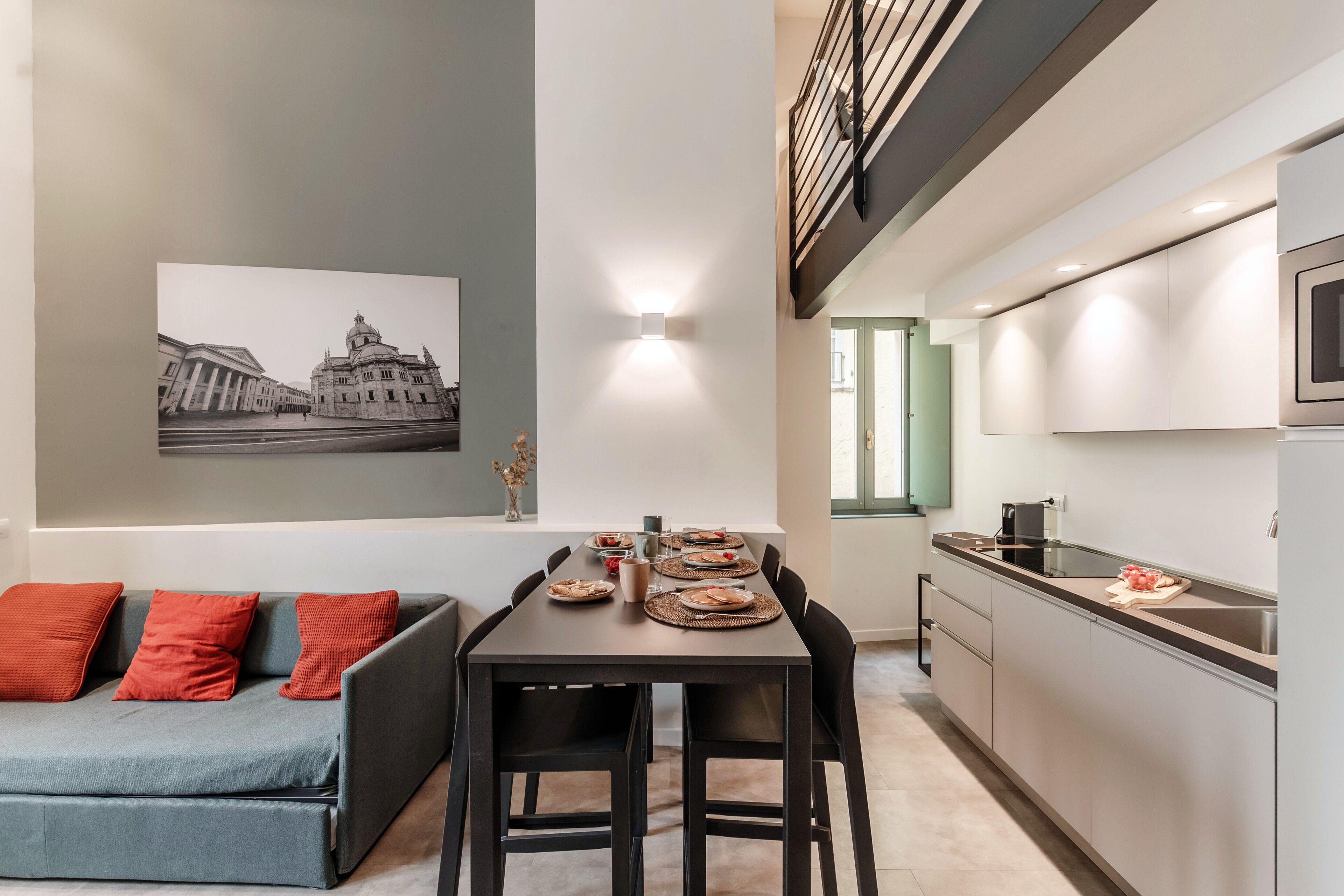 A modern kitchen with a dining area, a sofa with red cushions, and a framed picture on the wall.