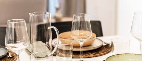 A dining table set with clear glassware and plates, with a wicker placemat and a bowl visible.