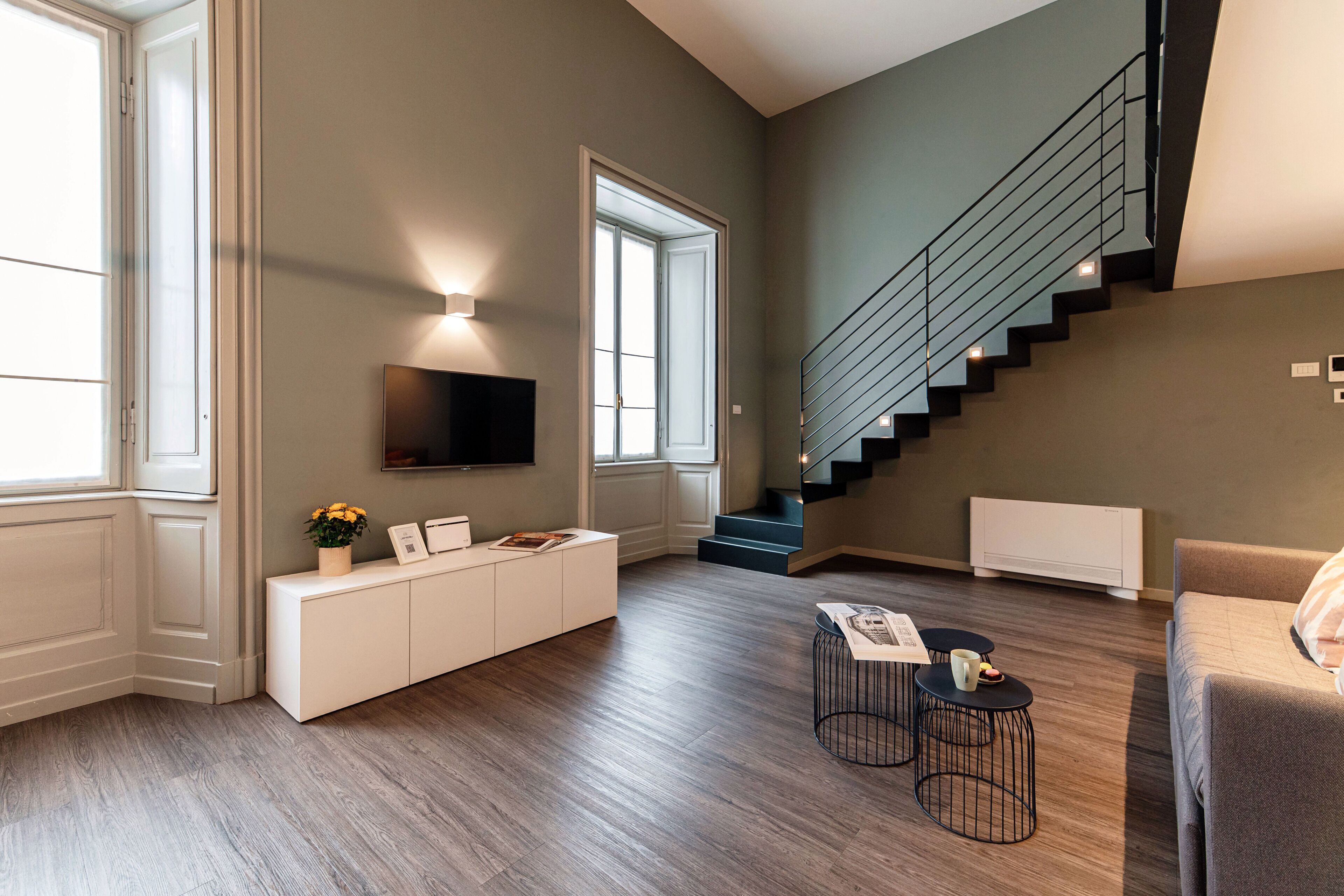 A modern living room with a staircase, a flat-screen TV, a white console, and a coffee table.
