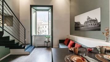 Un interno moderno con una scala, un'area pranzo con tavolo apparecchiato per la colazione e un'ampia finestra vista edifici.