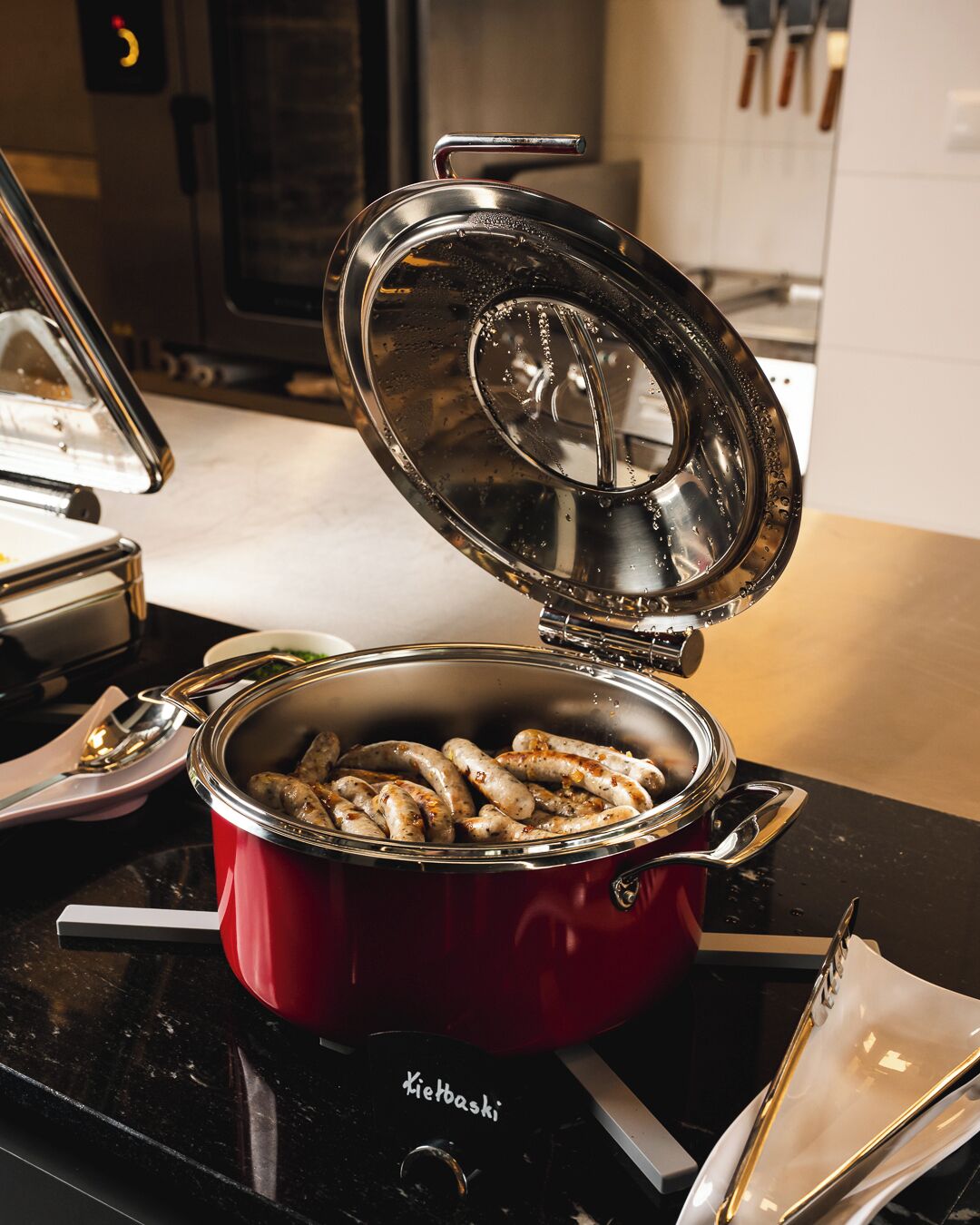 A red pot with sausages on a stove, a spoon, and a napkin on the counter.