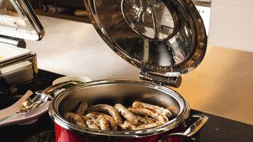 A red pot with sausages on a stove, a spoon, and a napkin on the counter.