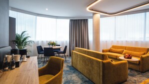 A modern hotel room with a sofa, dining table, chairs, and a potted plant. - Focus Hotel Premium Wrocław (Wroclaw)