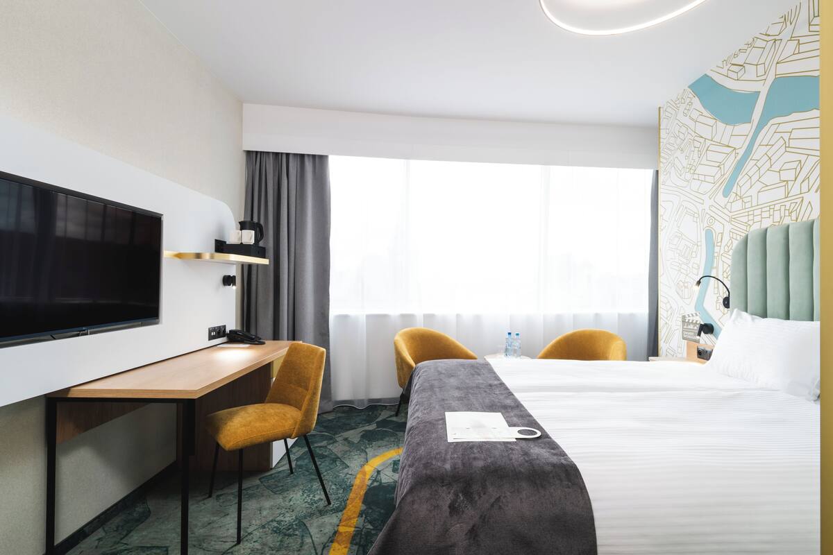 A hotel room with a bed, a desk with a chair, a television, and a map on the wall.