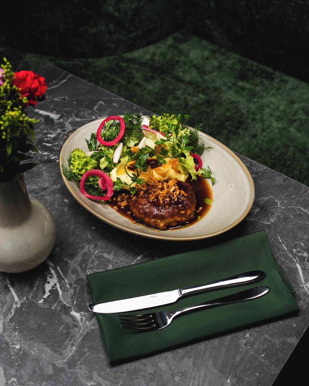 A plate of food with a green napkin and silverware on a dark marble table.