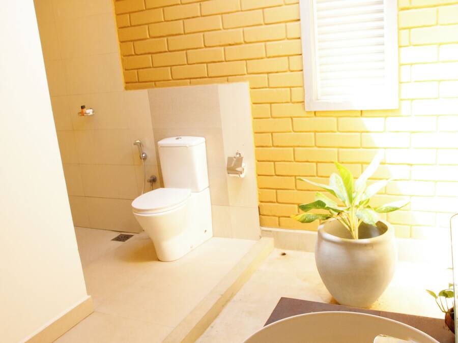 A bathroom with a white sink, a potted plant, and a toilet against a yellow brick wall.