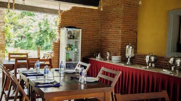 A dining area with brick walls, wooden tables, and chairs. There are water bottles, plates, and cutlery on the tables.