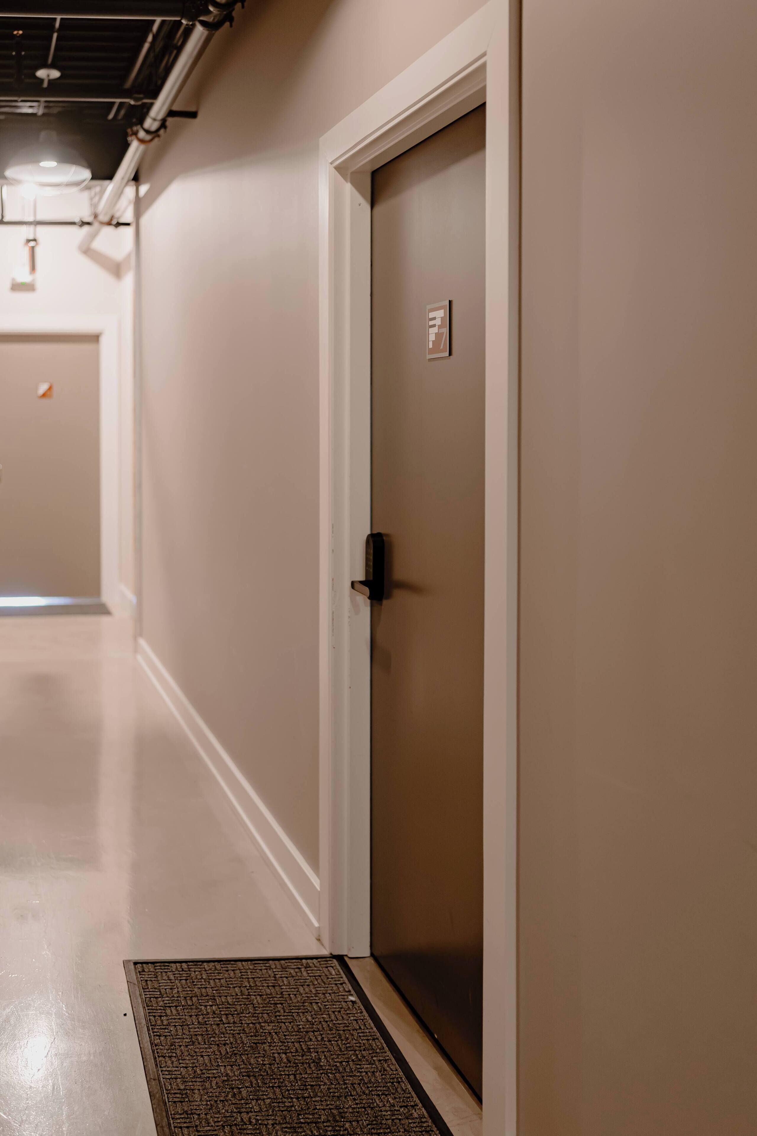 A hallway with a door, a doormat, and a wall-mounted sign.