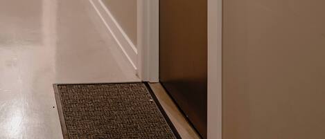 A hallway with a door, a doormat, and a wall-mounted sign.