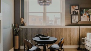 A dining area with a round table, two chairs, a vase with flowers, and a window with a view of buildings. - Modern Industrial Loft for Two (Benton Harbor)