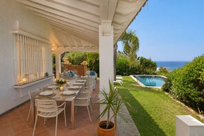 Un área de comedor al aire libre con piscina y vista al océano.