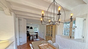 A dining area with a long table, white wicker chairs, a wooden buffet tray, and a chandelier. - Recently renovated villa overlooking the coast of Atlanterra, for 8 pax. (Tarifa)