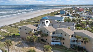 Un quartier résidentiel situé sur la côte, avec des propriétés donnant sur la plage, notamment une maison à deux étages dotée d’un balcon et d’une petite dépendance attenante.