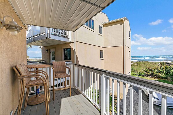 A balcony with wicker furniture, a white railing, and a view of the ocean.